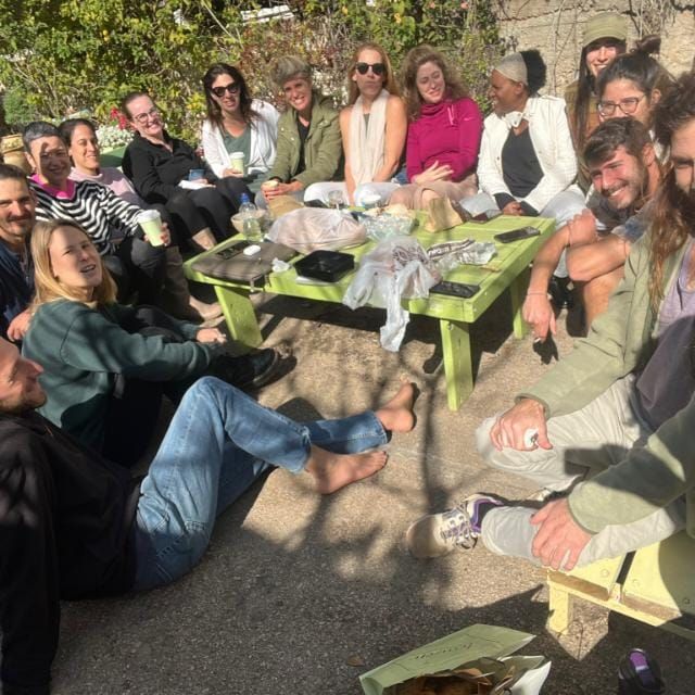 משתתפי הכשרת המטפלים יושבים יחד בחוץ סביב שולחן ומחייכים